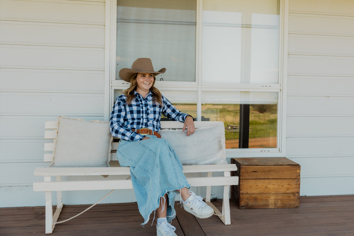 Woman in a navy check shirt and wide brim hat sitting on a verandah bench